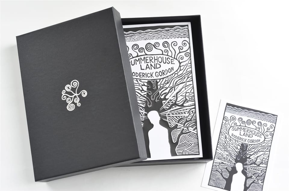 The open box with the jacketed hardback seated inside, lid and postcard alongside.