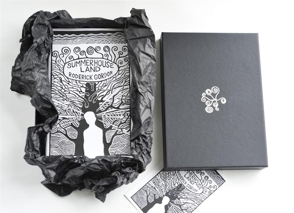 The book emerging from black tissue paper inside its box, with the postcard and lid beside it.